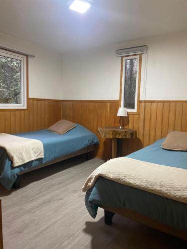 a room with two beds and a table and two windows at Aldea Molco Arrayan in Villarrica