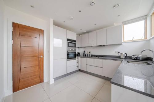 a kitchen with white cabinets and a wooden door at Elegant One Bed Penthouse with Terrace in London