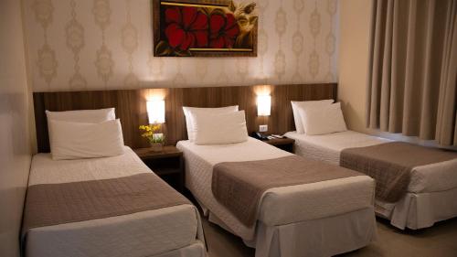 Una habitación de hotel con tres camas y un cuadro en la pared. en Pietro Angelo Hotel, en Foz do Iguaçu