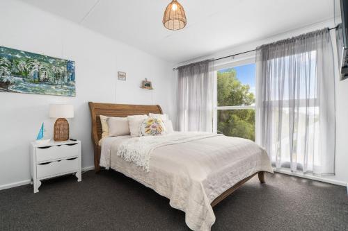 een witte slaapkamer met een bed en een raam bij Whispers of Sunset in Dromana