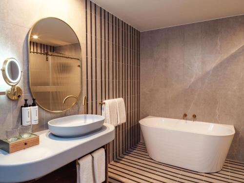 a bathroom with a tub and a sink and a mirror at voco Gosford by IHG in Gosford