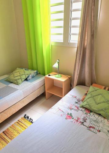 a bedroom with two beds and a window and a lamp at T3 Serenity aux couleurs du soleil à Ducos in Ducos
