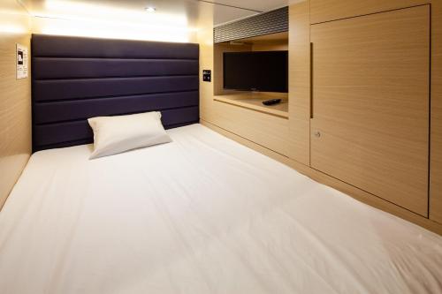 a room with a bed with a tv and a wall at Y's CABIN&HOTEL Naha Kokusai Street in Naha