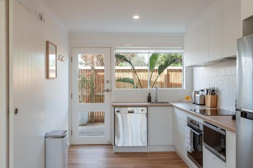 a white kitchen with a sink and a window at Magpie Sands - Ocean Views & Seaside Luxury - Steps to beach in Aldinga Beach