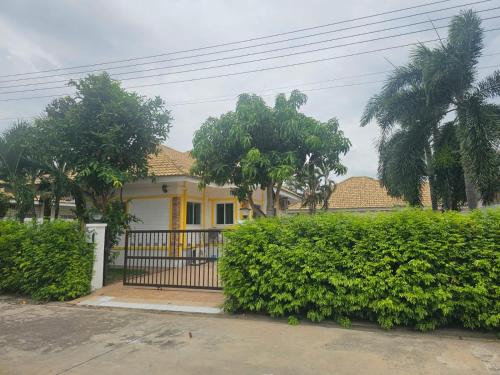een geel huis met een hek voor een heg bij Barn sabai pool villa in Ban Wang Phong