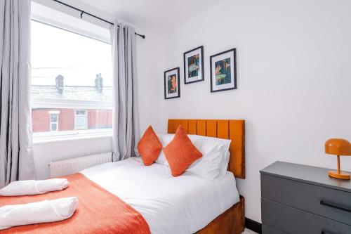a bedroom with a bed with orange pillows and a window at Bright & Spacious 4-Bed Home in Darwen Town by Eason Stays, Perfect for Contractors, Business Travellers & Groups - with Free Parking! in Darwen