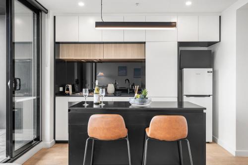 a kitchen with a black island with two chairs at Luxe High-Floor Retreat- Epic Views-Steps to Crown in Melbourne