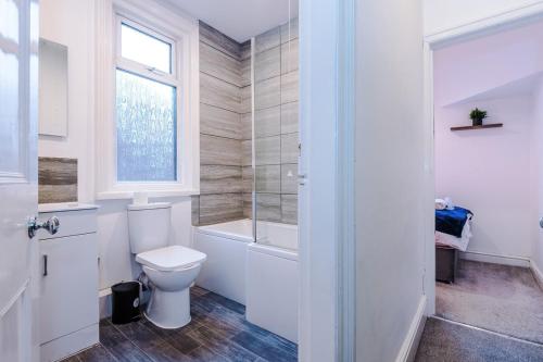 La salle de bains est pourvue de toilettes, d'une baignoire et d'une fenêtre. dans l'établissement Four BR House By Eason Stays Short Lets & Serviced Accommodation Worsley With Free Parking, à Worsley