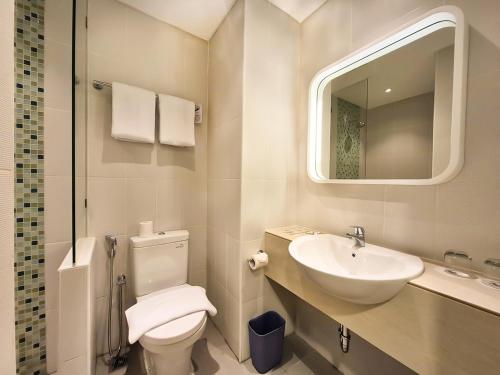 a bathroom with a toilet and a sink and a mirror at Zest Ambon by Swiss-Belhotel International in Ambon