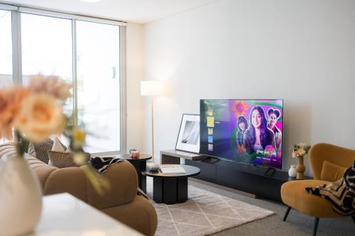a living room with a flat screen tv and chairs at Gorgeous 3BR,2Parking,Pool,Gym,near Airport and City in Sydney