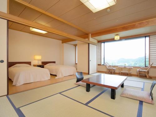 a room with two beds and a table and a window at Yamamura Bekkan in Nagato