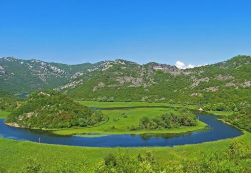 an island in a river with mountains in the background at Estate & Winery San Duyevo in Rijeka Crnojevića