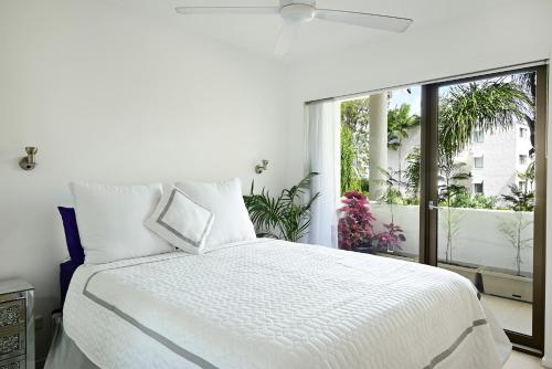 a white bedroom with a bed and a large window at St Tropez 8 - Waterfront Retreat with Rooftop Spa & Sauna in Noosa Heads
