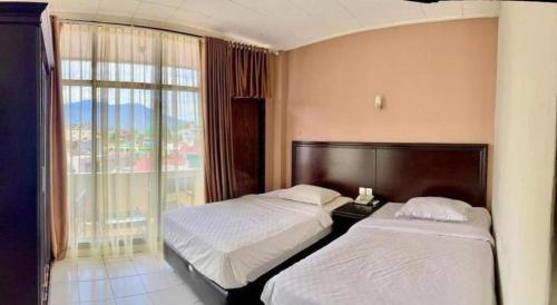 two beds in a hotel room with a window at Hotel Benteng in Bukittinggi