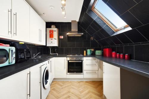 a kitchen with white cabinets and a black tile wall at 3-Bedroom 5-Bed Flat King Room Free Parking Near Reading & M4 Work Stays in Shinfield
