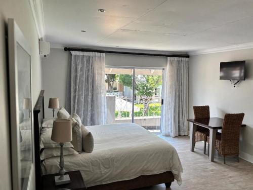 a bedroom with a bed and a desk and a window at Bateleur Guesthouse in Klerksdorp