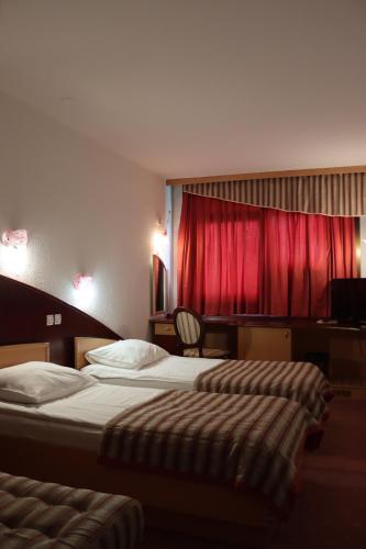 two beds in a hotel room with a red curtain at MC Hotel in Žalec