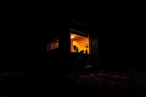 a person sitting in a chair in a window at night at Homnest - Refuge en nature au coeur du Tarn in Puybegon