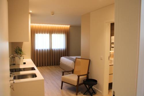 a room with a bed and a chair and a kitchen at ma-la studios Guimarães in Guimarães