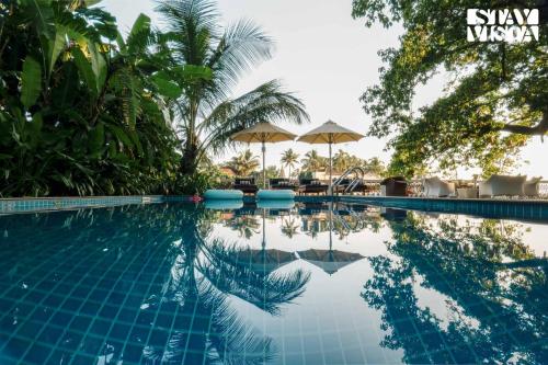 una piscina con palmeras y sombrillas en StayVista at Di Mora by the Sea with Lawn & Pool, en Baga