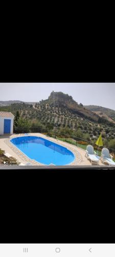 a large swimming pool with two chairs and an umbrella at Alojamiento rural El Yate in Montefrío