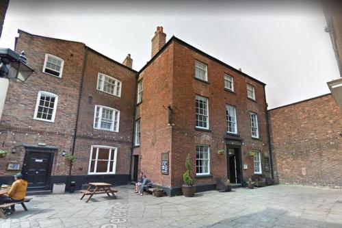a large brick building with people sitting on benches in front at The Commercial Bar & Hotel in Chester