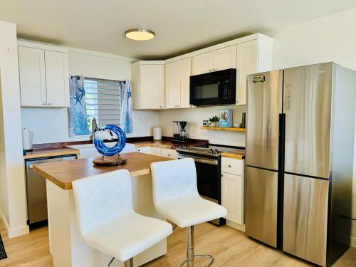 a kitchen with a refrigerator and two white chairs at Island Glow Kailua Village #508 free assigned parking, AC, downtown, walk to restaurants, bars and the pier in Kailua-Kona
