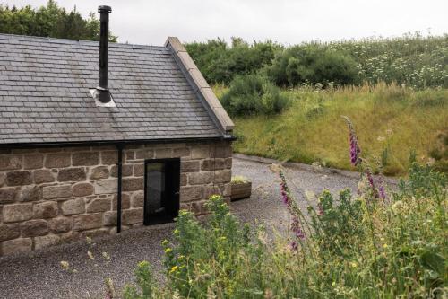a stone building with a door in a garden at Burnside Cottage By Birch Stays in Stonehaven