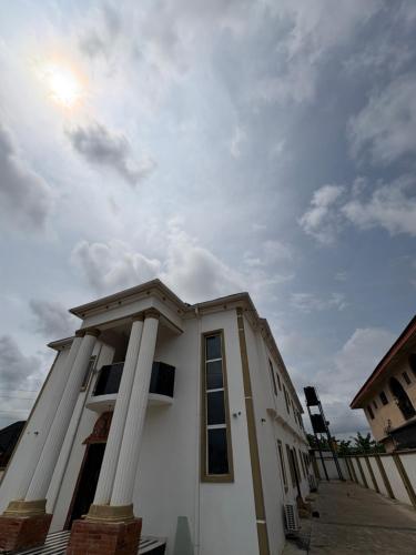 a white building with columns and a cloudy sky at Hog Inn Hotel in Benin City
