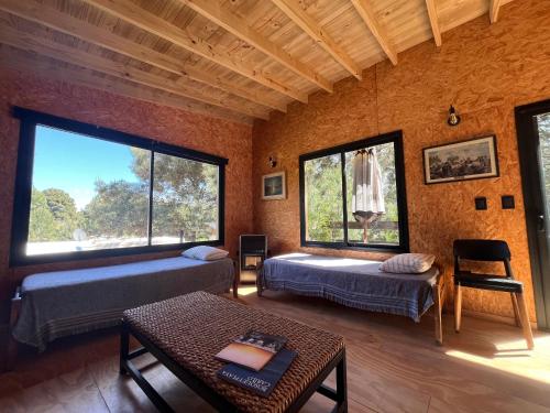 ein Zimmer mit zwei Betten und einem Tisch und Fenstern in der Unterkunft Cabaña Meliades - Bosque & Calma en Familia - Ayres Del Bosque Alojamientos in Ostende