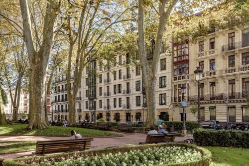 people sitting on benches in a park in front of a building at Batimont Suites & Apartments in Bilbao
