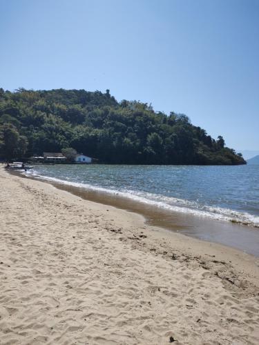 a sandy beach with water and trees in the background at Pousada Dádiva girassol encantado Pontal Centro in Paraty