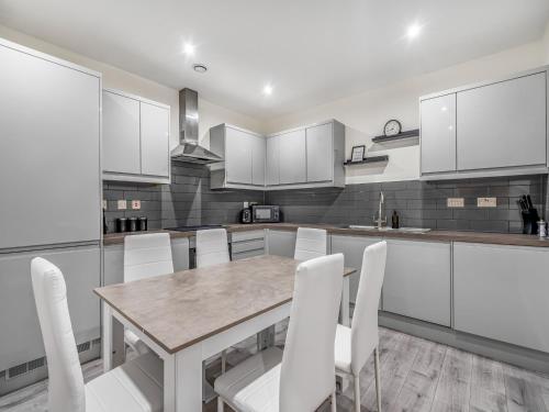 a kitchen with white cabinets and a wooden table and chairs at The Calm Quarters - City Centre 2BR 2BA in Leicester