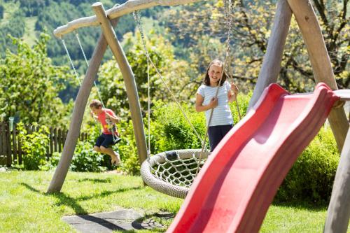 two children playing on a swing set in a yard at Großplonerhof in Luson