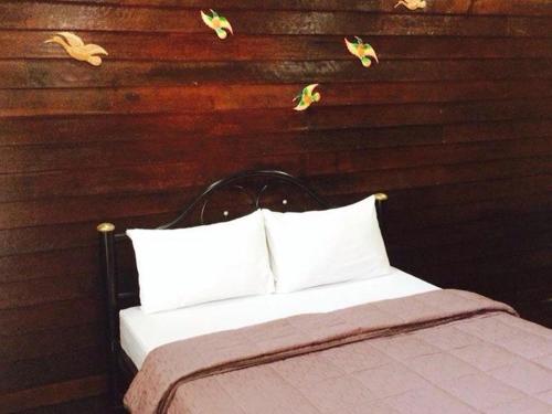 a bed with white pillows in front of a wooden wall at K Guesthouse Adults only in Krabi town