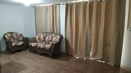 two chairs in a living room with curtains at A home away from home in Ijuí