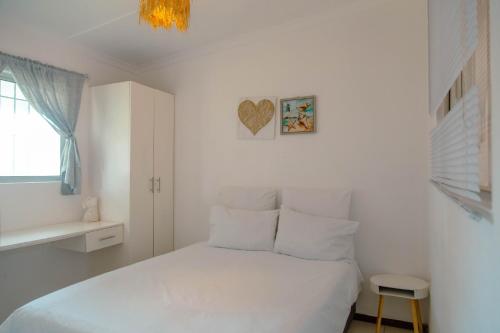 a bedroom with a white bed with a heart picture on the wall at The Ocean Side Cottage in Cape Town