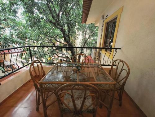 a glass table and chairs on a balcony with a tree at Navilehomestay in Candolim