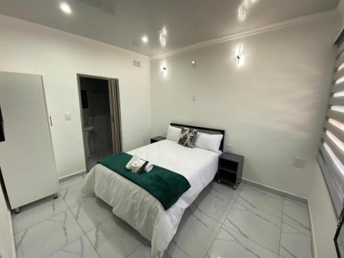 a white bedroom with a bed with a green blanket at The Palms Guest House in Johannesburg