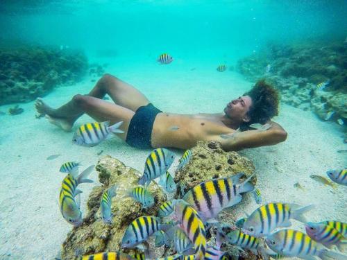 a man laying in the water next to some fish at Casa Miss Paripueira in Paripueira
