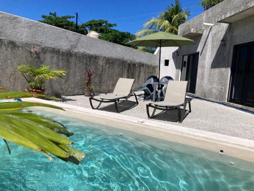 Dos sillas y una sombrilla junto a una piscina. en Casa Arena Cozumel, en Cozumel