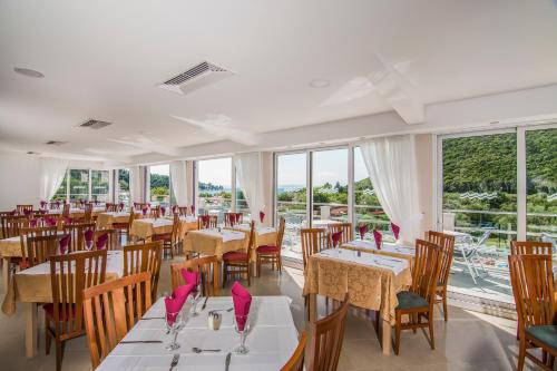 un comedor con mesas, sillas y ventanas en Hotel Hedera - Maslinica Hotels & Resorts, en Rabac