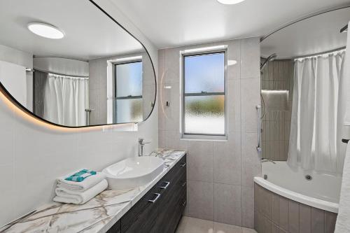 a bathroom with a sink and a tub and a mirror at Grand Palais Boolarong Beachside Apartments in Alexandra Headland