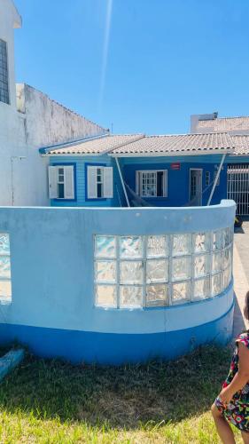 a little girl sitting next to a blue house at Casa com piscina perto da praia in Rio Grande