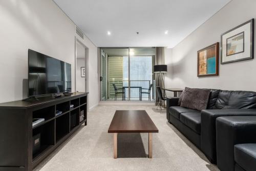 a living room with a black couch and a flat screen tv at 2-Bed City Retreat with Gym and Pool Access in Adelaide