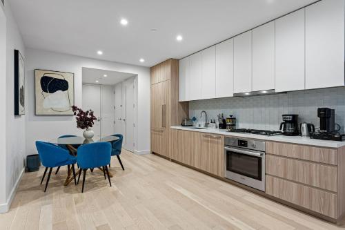 a kitchen with wooden cabinets and a table and blue chairs at Pearl Coast - Modern 2BR with Rooftop Pool & Views in Los Angeles