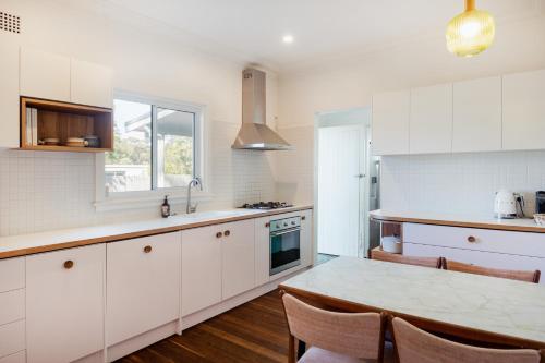 a kitchen with white cabinets and a table with chairs at The Blue Beach House - Pet Friendly Coastal Escape in Mollymook in Mollymook