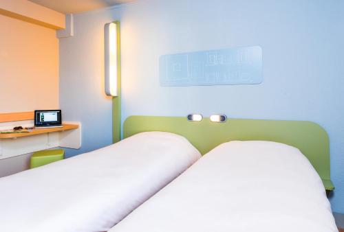 a room with a bed and a desk with a laptop at ibis Budget Courbevoie Paris La Défense in Courbevoie