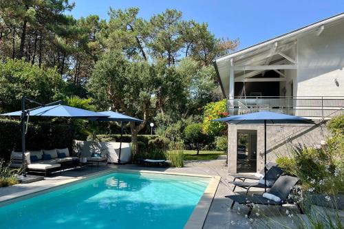 a swimming pool with two umbrellas and a house at Villa Hortensia - Welkeys in Soorts-Hossegor