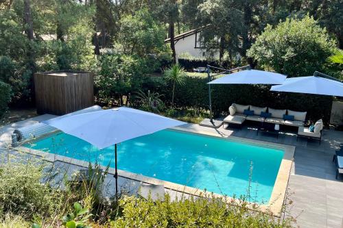 a pool with two umbrellas and a couch and a table at Villa Hortensia - Welkeys in Soorts-Hossegor